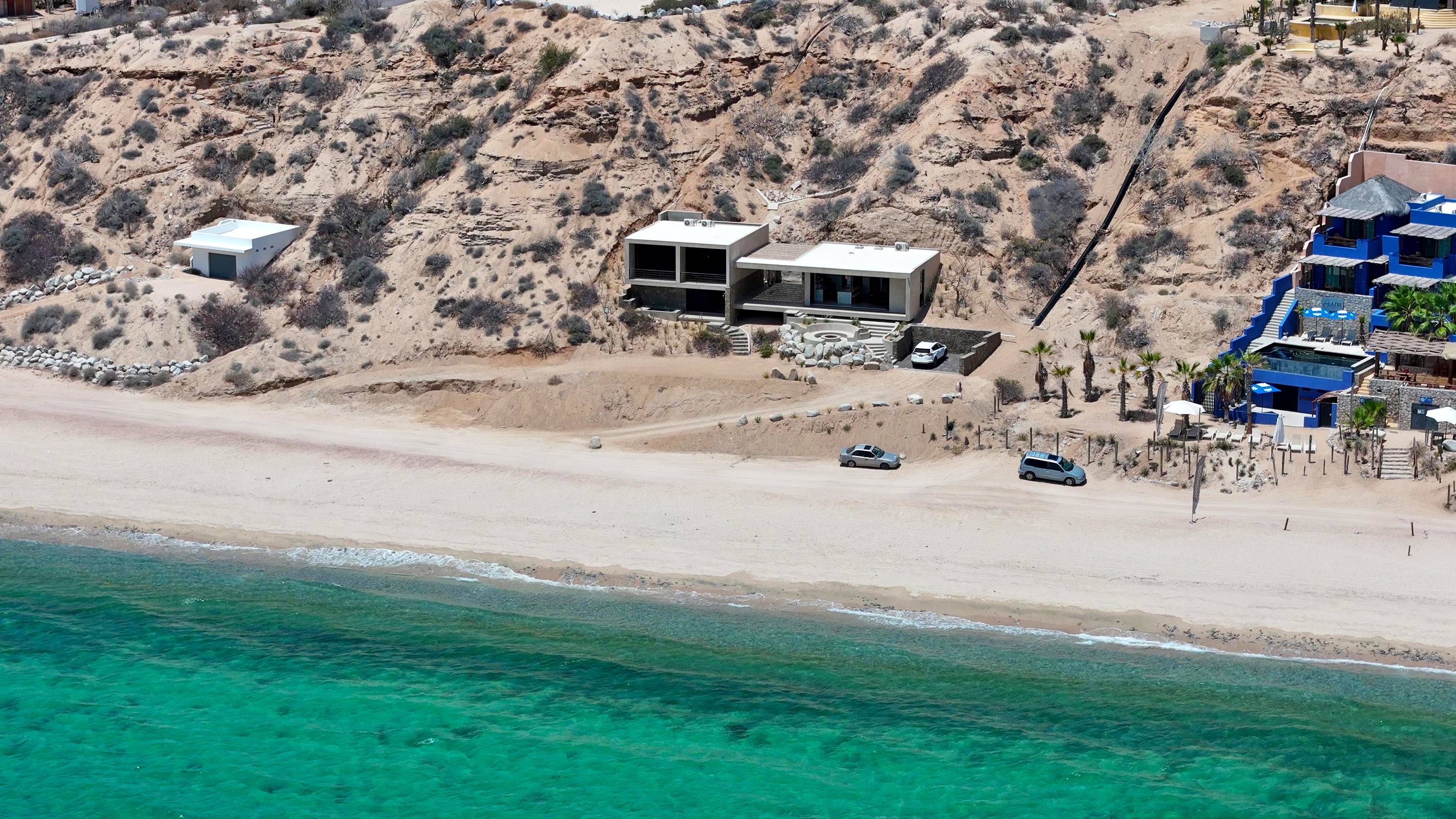 The beach below the house from the air, buildings along the low bluff.
