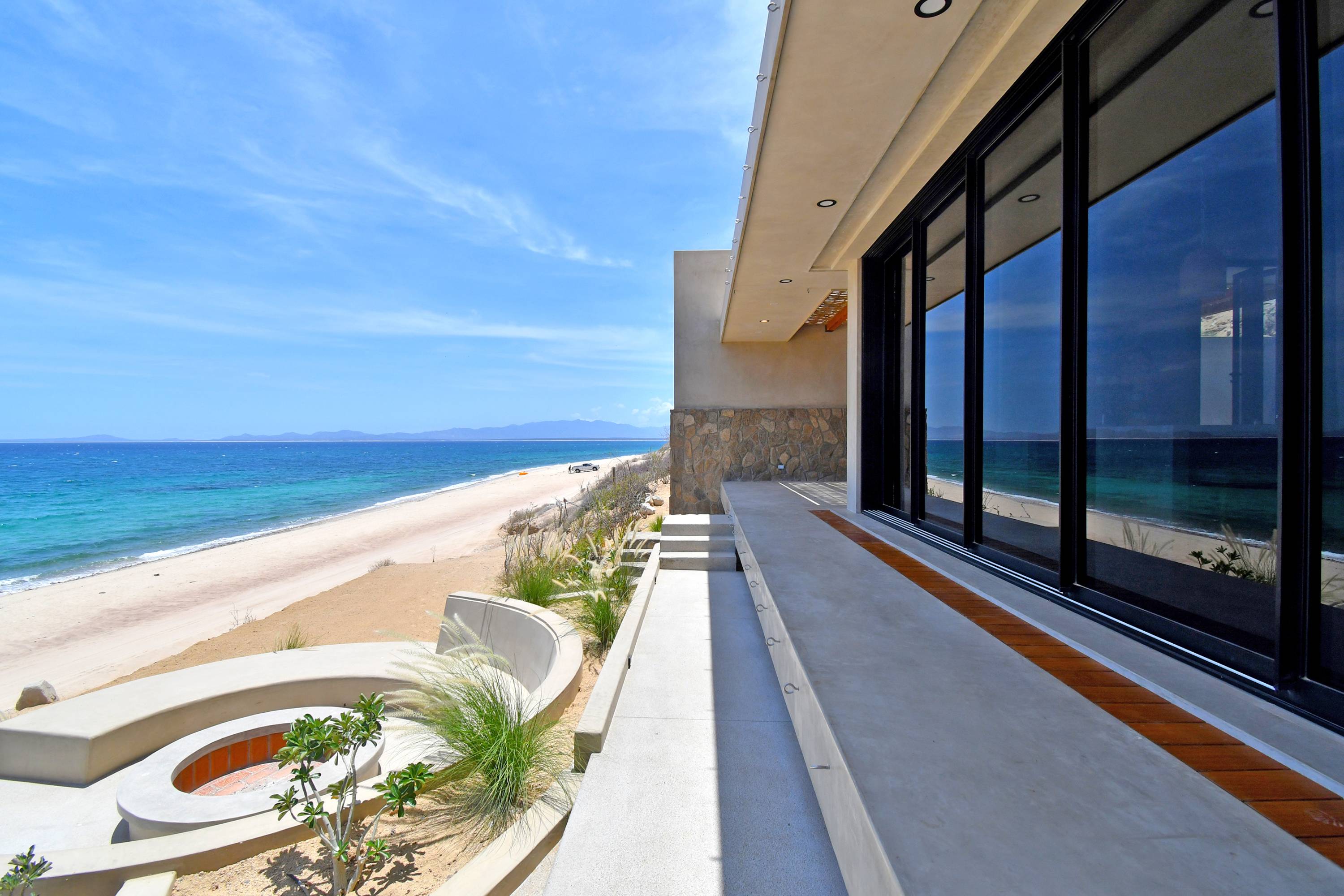 The walkway along the front of the house, fire pit at the left and the bay beyond.