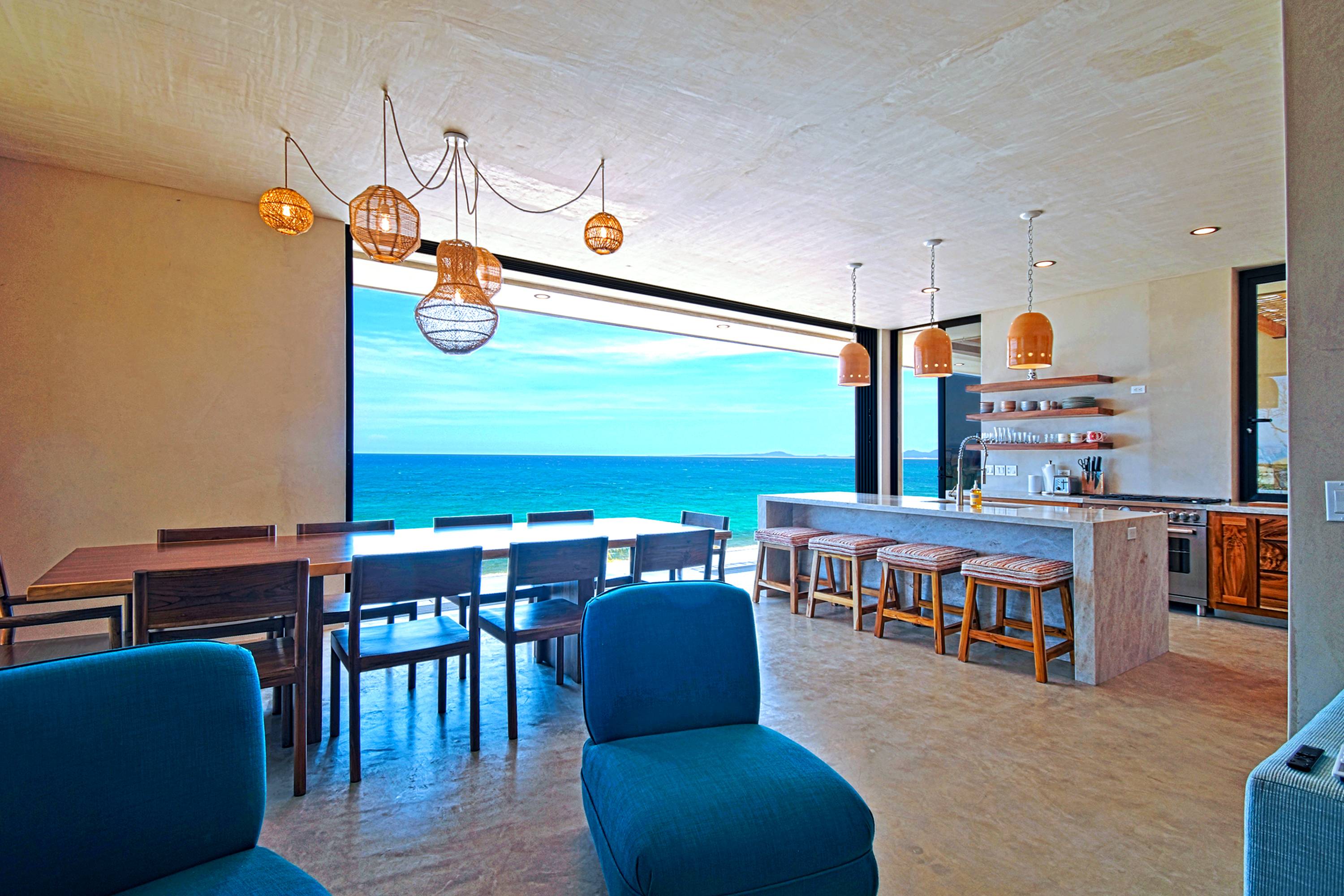 The living side from the sitting area, teak dining table and kitchen island with the glass front open to the bay.