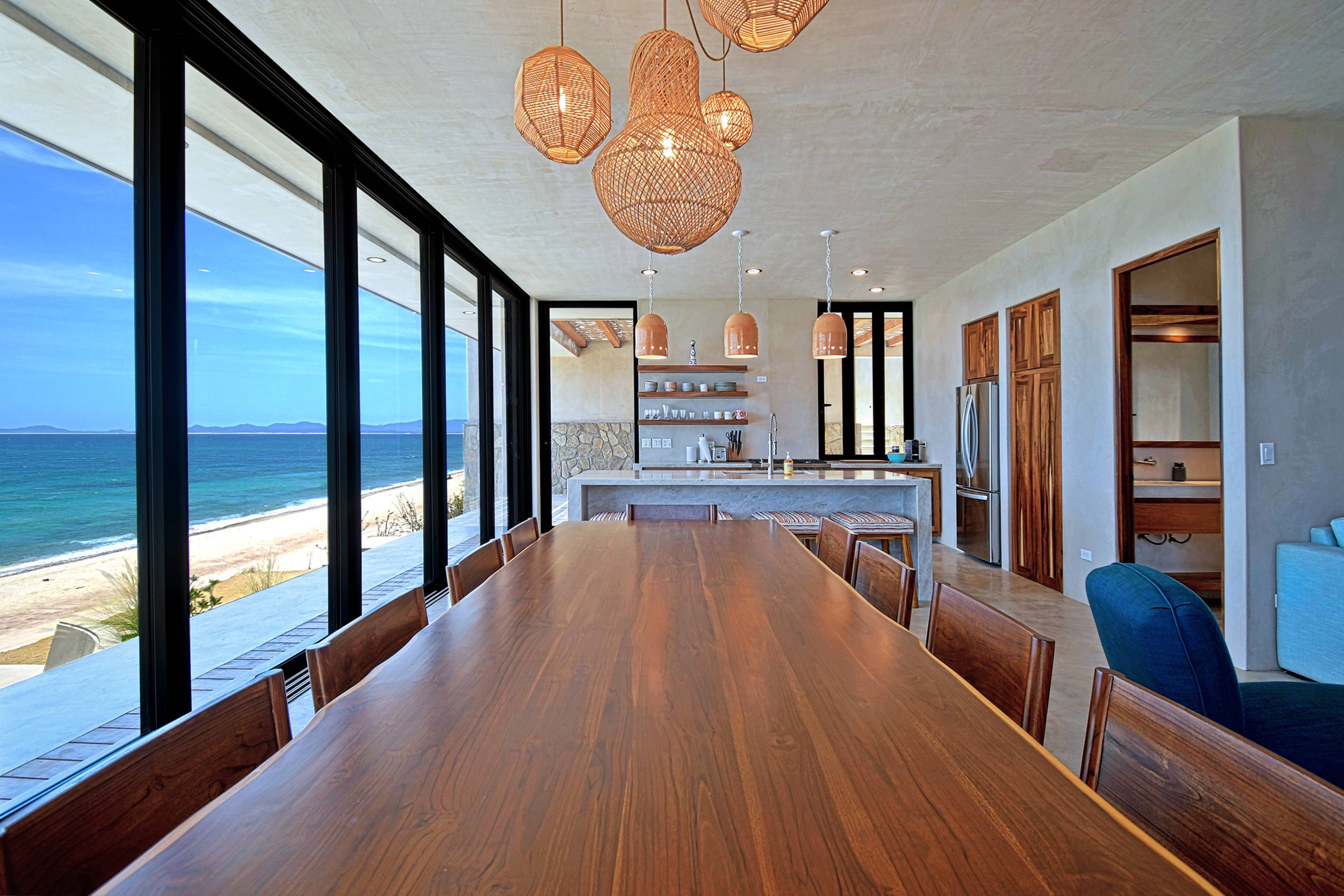 The teak dining table running toward the kitchen, glass wall along the front.