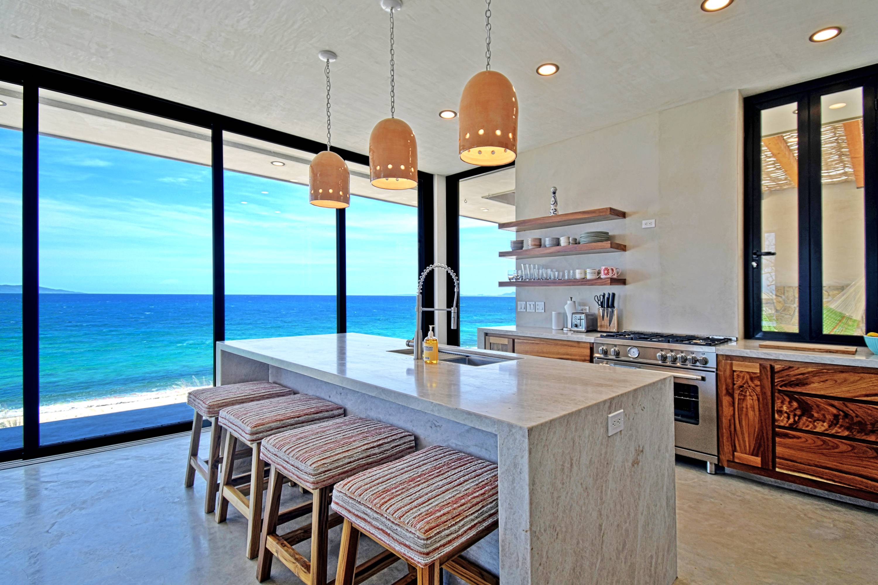 Bar stools along the kitchen island, range and open shelving behind.